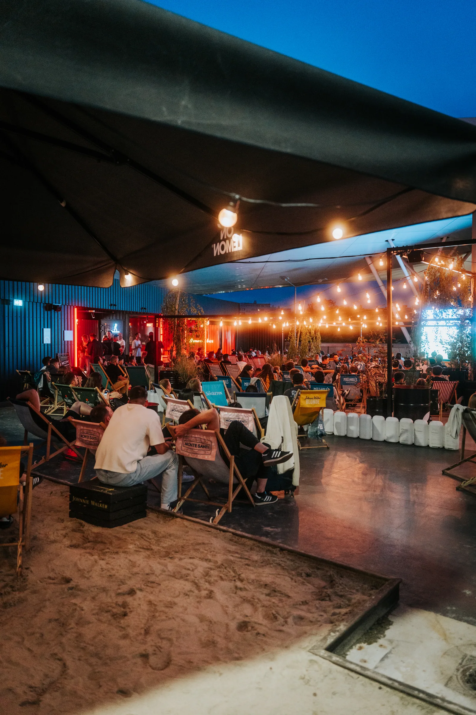 Goście i oświetlona przestrzeń Pitlane Summer Bar nocą